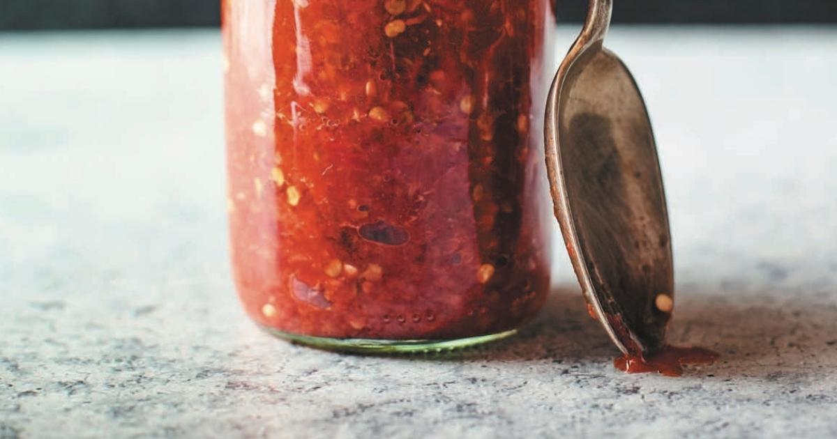 A clear jar filled with a red hot sauce.