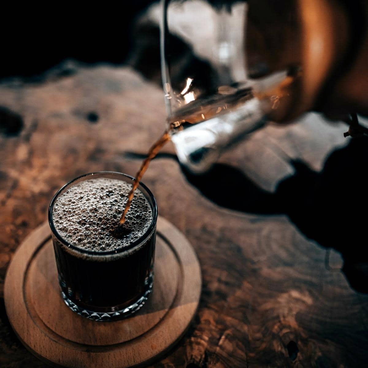 Dark coffee being poured into a clear glass.