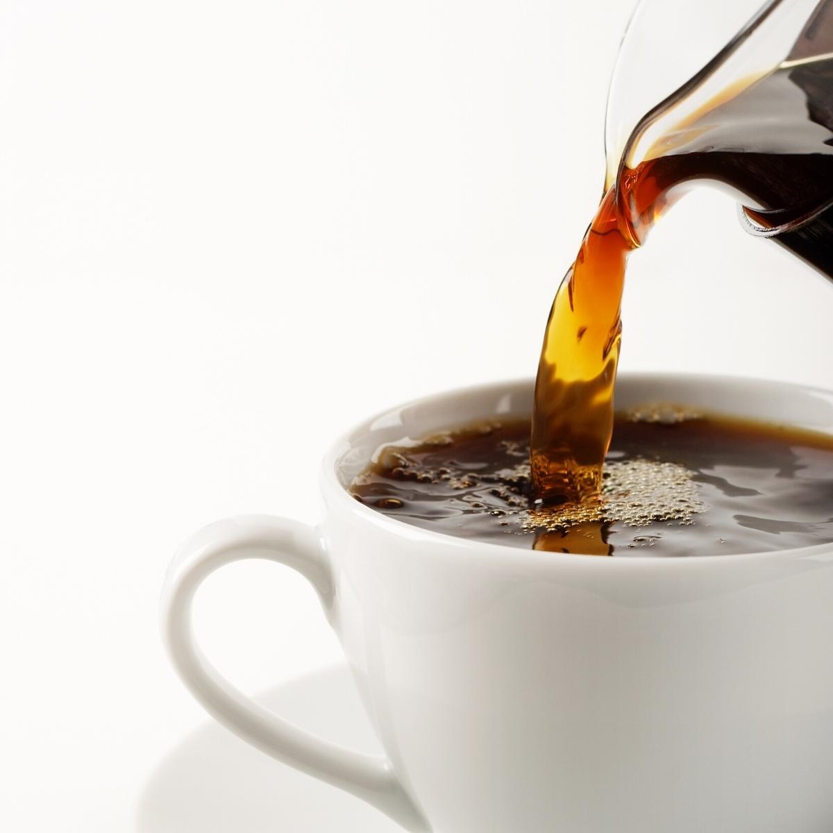 Coffee being poured into a white mug resting on a white saucer.