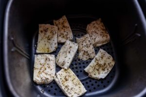 Cubes of seasoned tofu and succulent halloumi are placed in an air fryer basket, ready for cooking.
