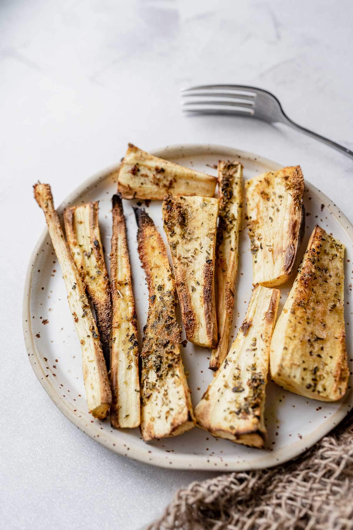 Air Fryer Parsnips on a stoneware plate, with a fork above.