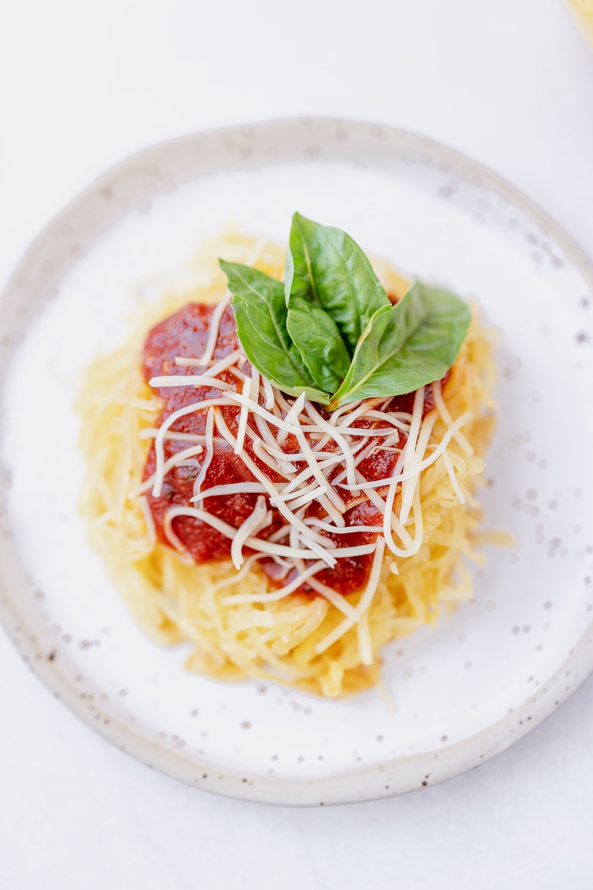 Overhead shot of Air Fryer spaghetti squash on a stoneware plate with marinara, parmesan and fresh basil on top.