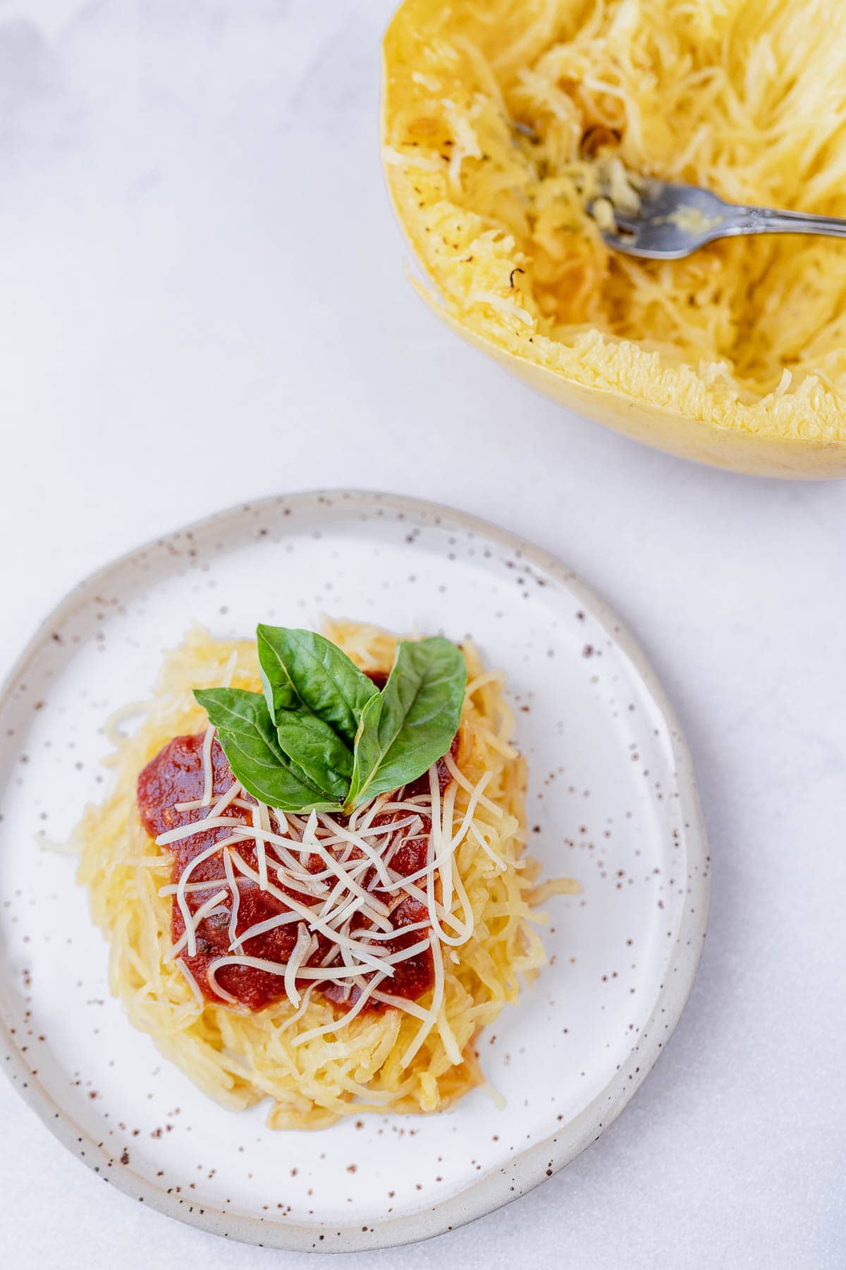 Overhead shot of Air Fryer spaghetti squash on a stoneware plate with marinara, parmesan and fresh basil on top, next to spaghetti squash with a fork.