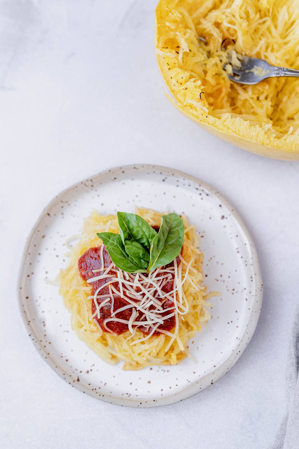 Overhead shot of Air Fryer spaghetti squash on a stoneware plate with marinara, parmesan and fresh basil on top, next to spaghetti squash with. a fork.