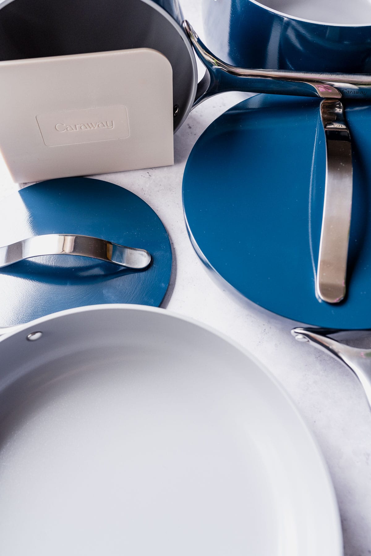 A navy colored Caraway cookware set  resting on a gray table.