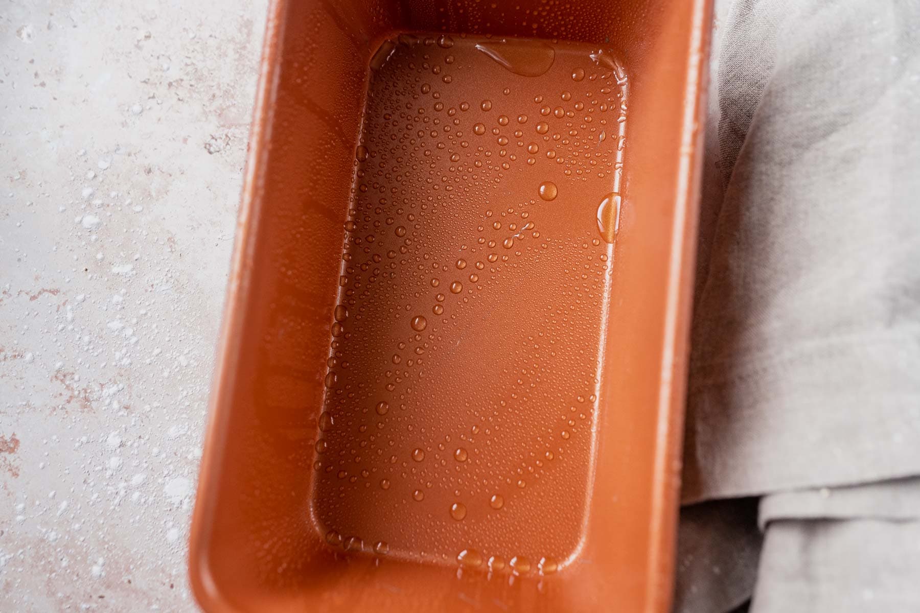 A copper cake loaf tin with droplets of oil.