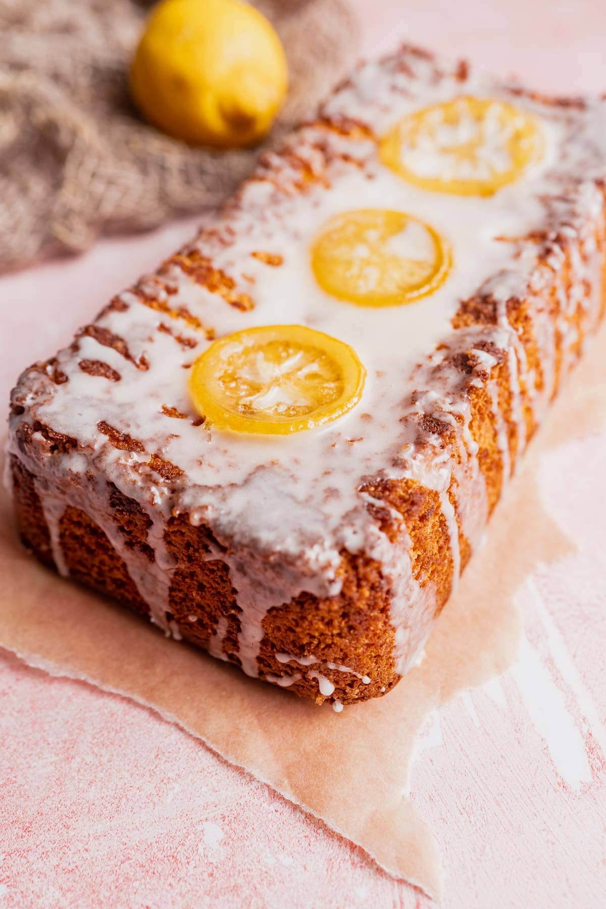 A dark yellow loaf cake drizzled with white glaze and topped with slices of lemon.