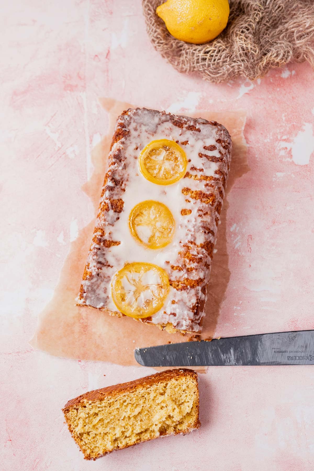 Top view of a yellow loaf cake drizzled with white glaze and candied lemon slices resting next to a black bread knife.