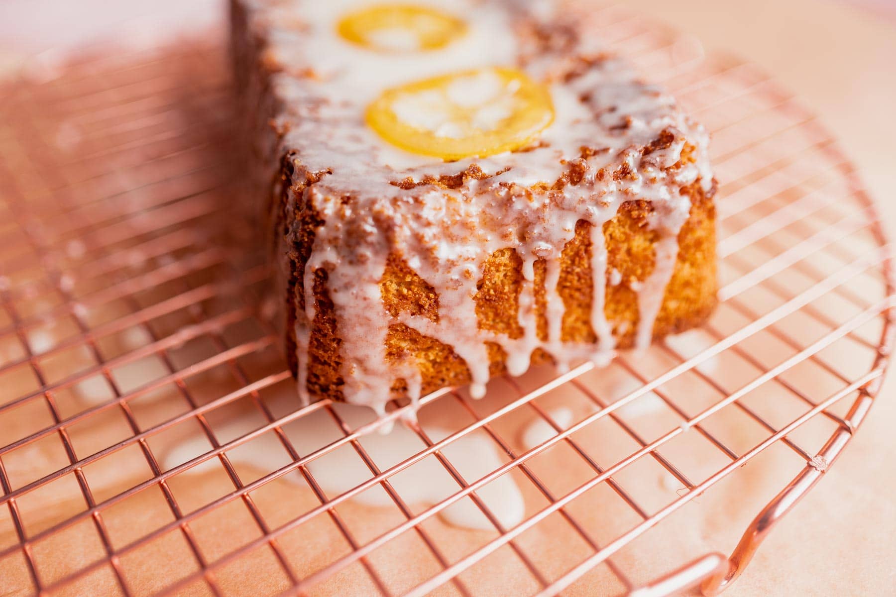 A loaf cake resting on a copper wire rack, drizzled with white icing and topped with candied lemon slices.