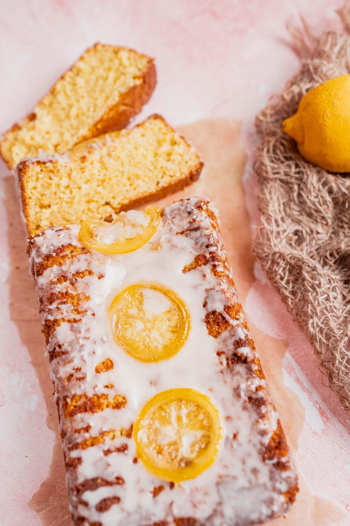 A sliced loaf cake topped with white icing and lemon slices.