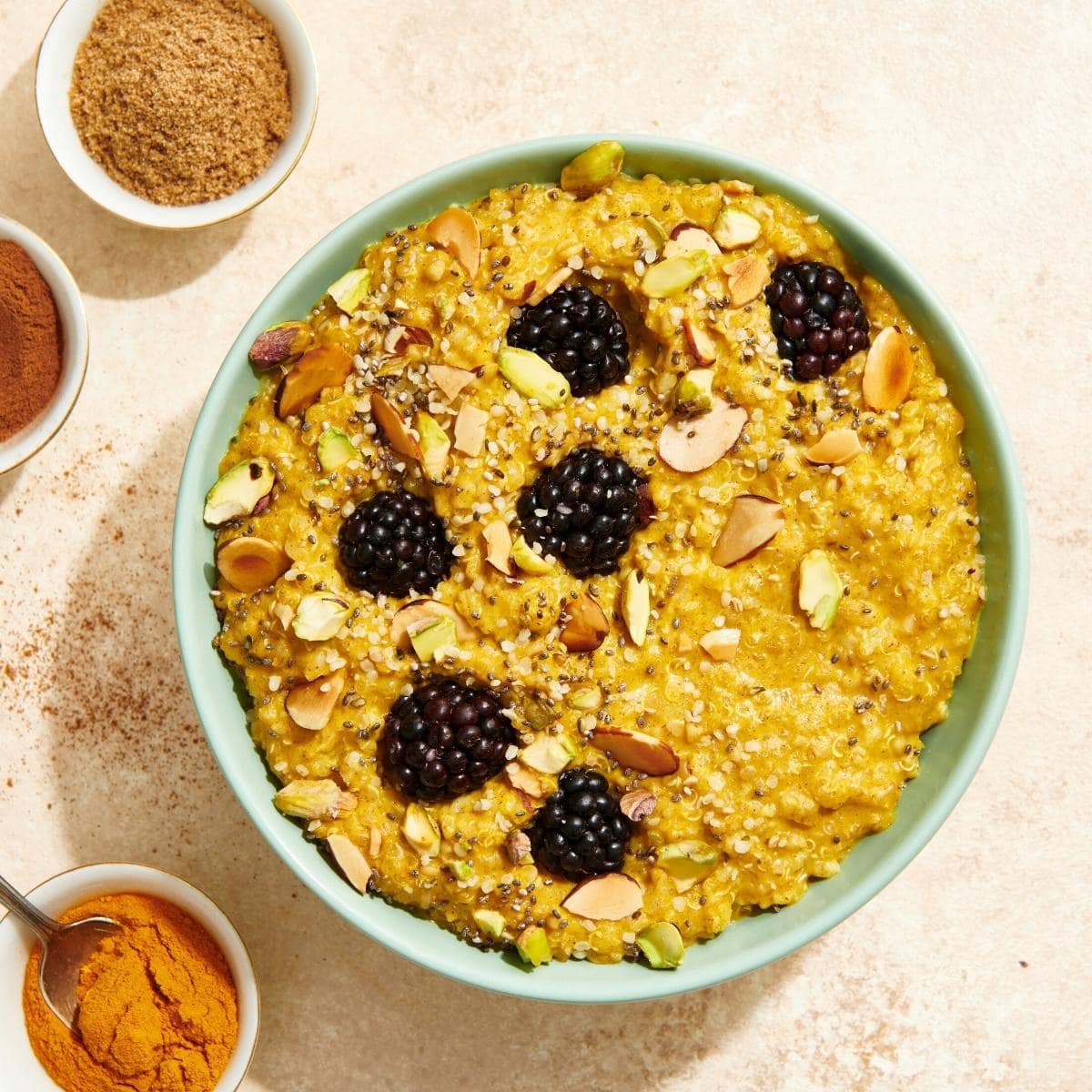 A green bowl filled with golden oatmeal topped with fresh blackberries.