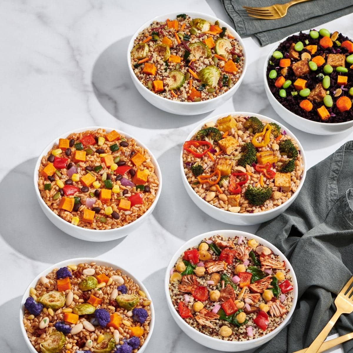 Several white bowls filled with colorful food resting on a white table.