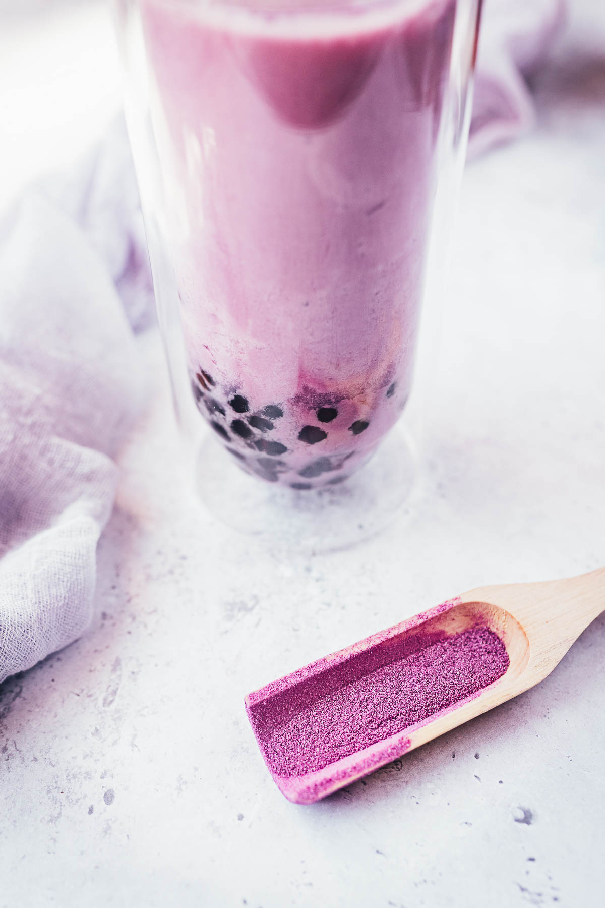 Taro Milk Tea in a clear glass with black tapioca pearls at the bottom, next to a scoop of purple taro powder.