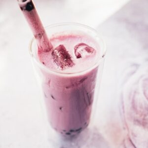 A big straw sticking out of a clear glass filled with purple liquid.