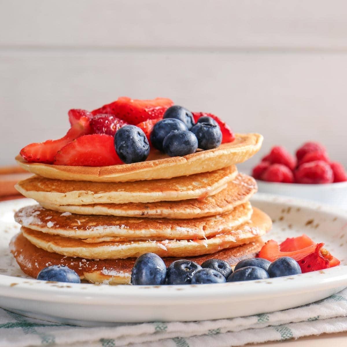 A stack of pancakes topped with fresh berries and shredded coconut.