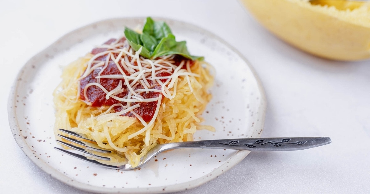 A ceramic plate with spaghetti squash covered in marinara sauce and parmesan cheese.