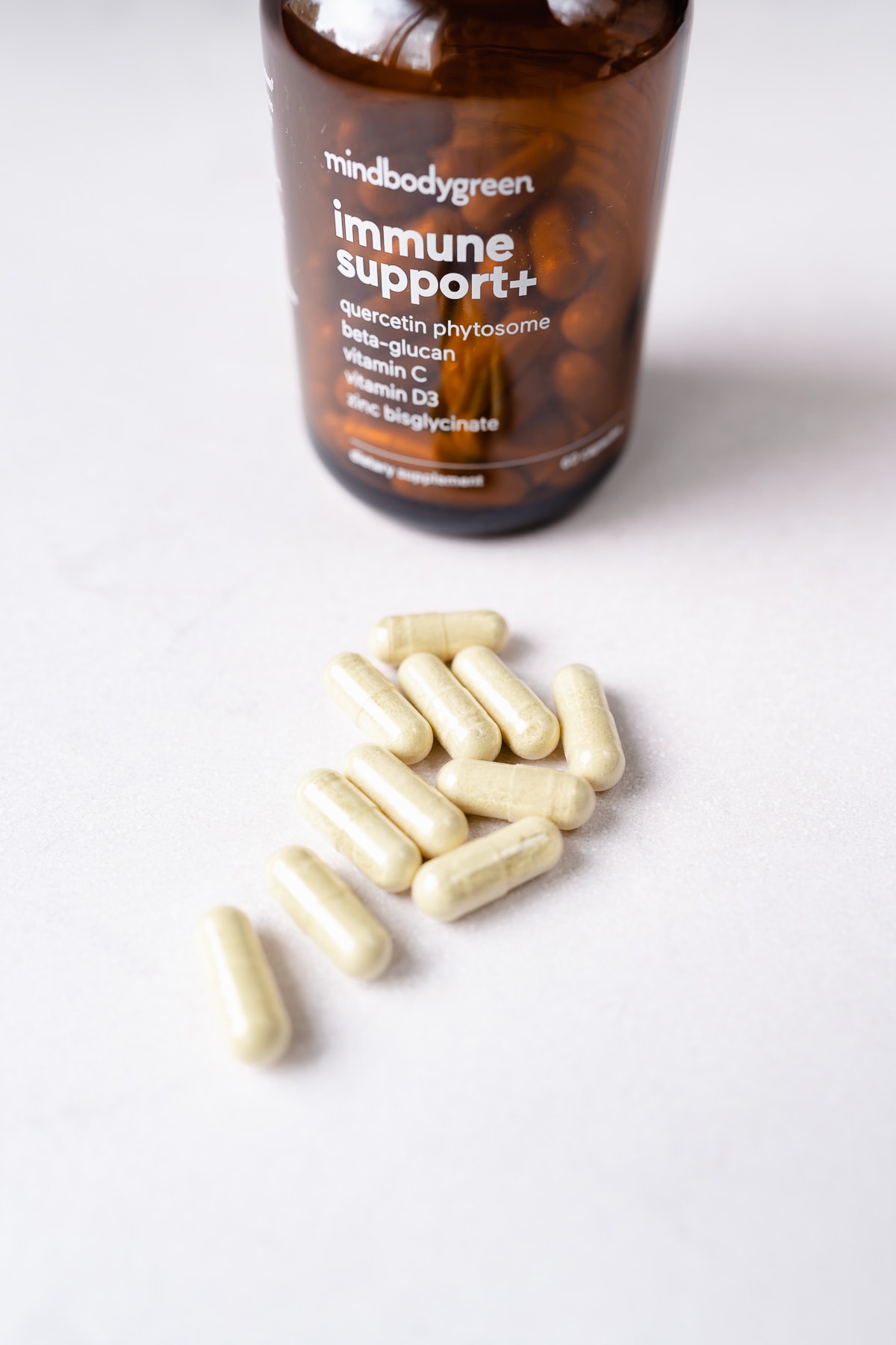 Light tan capsules rest on a white table next to a supplements bottle.