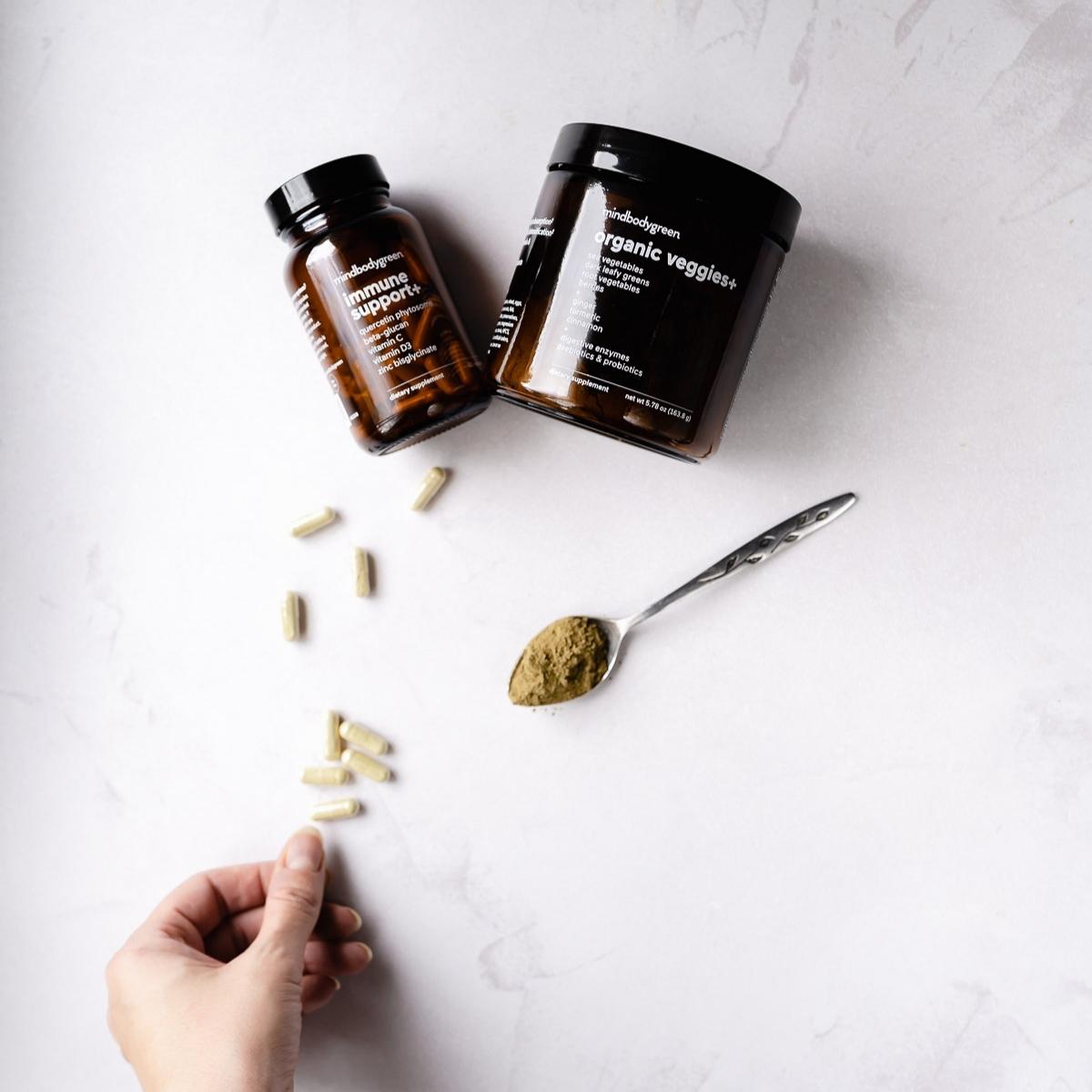 A hand reaches for a tan colored gel capsule resting next to dark brown containers of supplements.