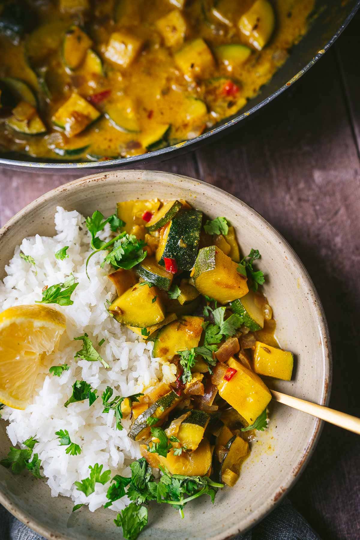 A gold spoon juts out of a ceramic bowl filled with squash curry served over rice with a lemon wedge.