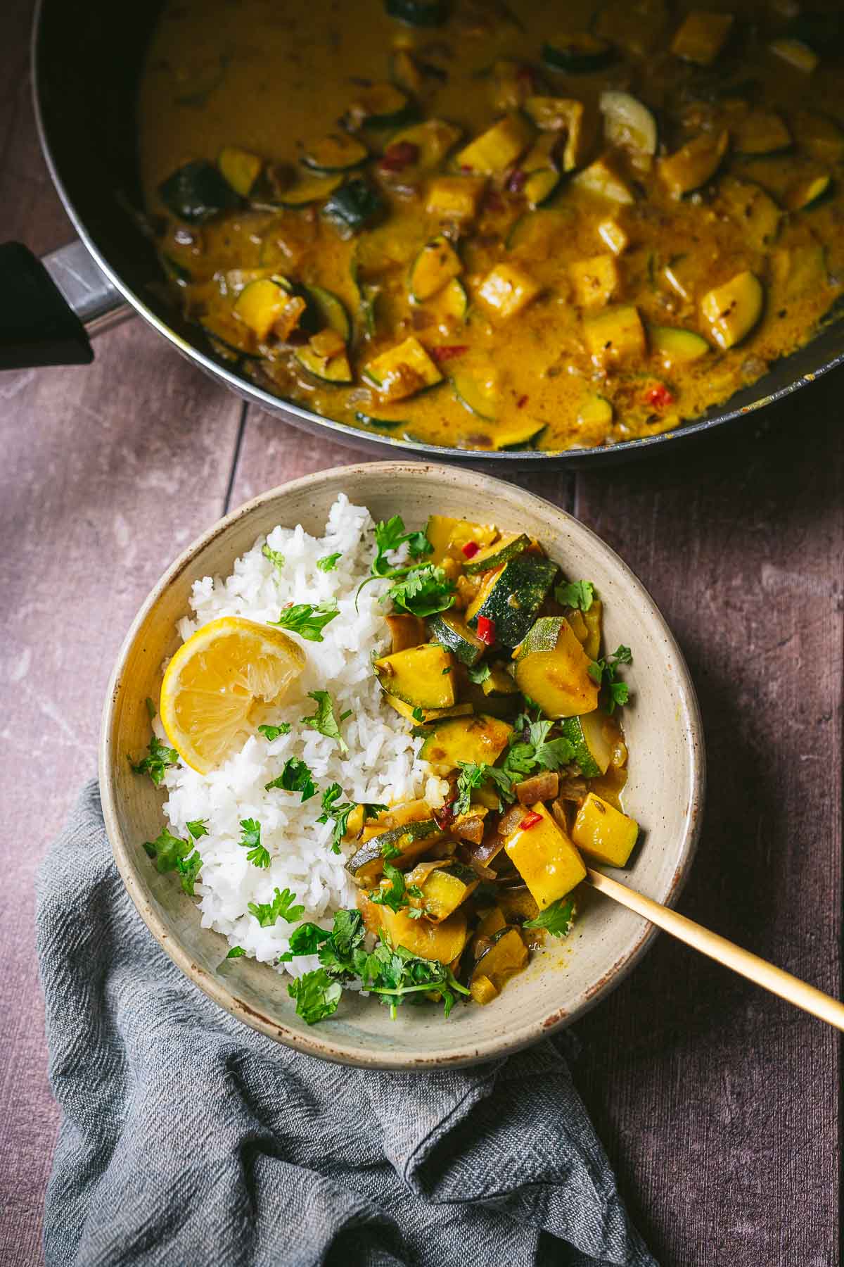 A bowl of curry and rice rests next to a large pan filled with curry.