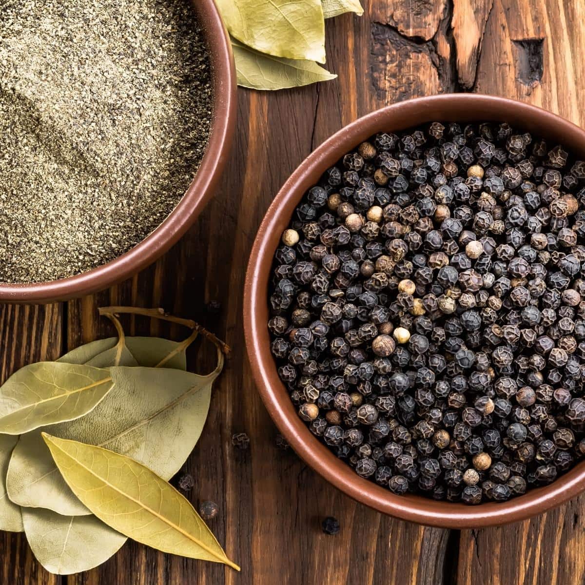 Black peppercorns and ground black pepper resting on a wood table.