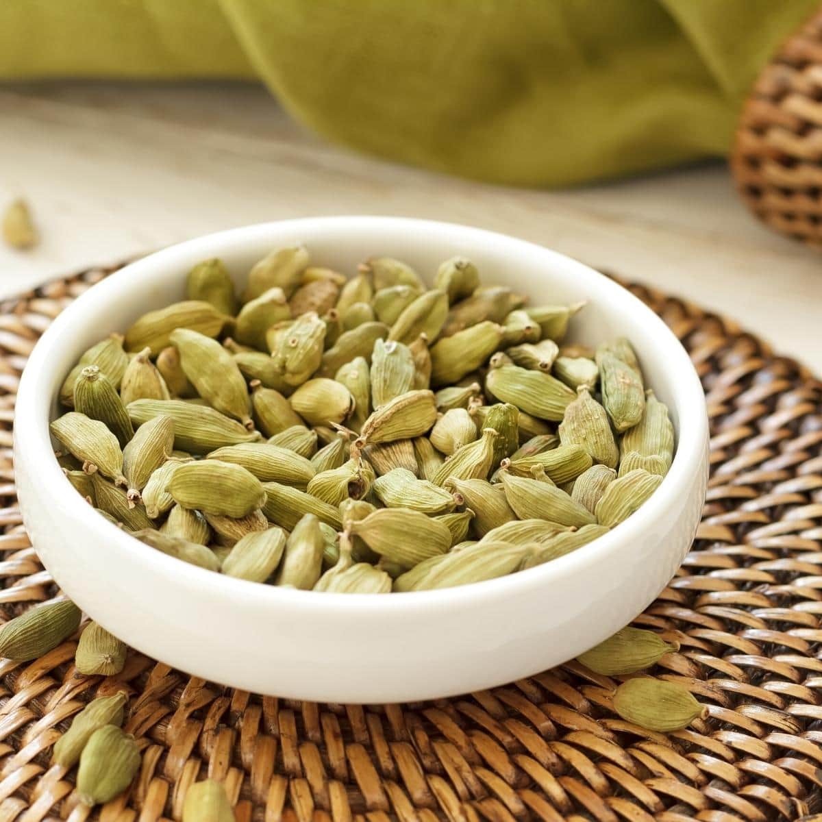 Green cardamom pods resting in a small white ceramic dish.