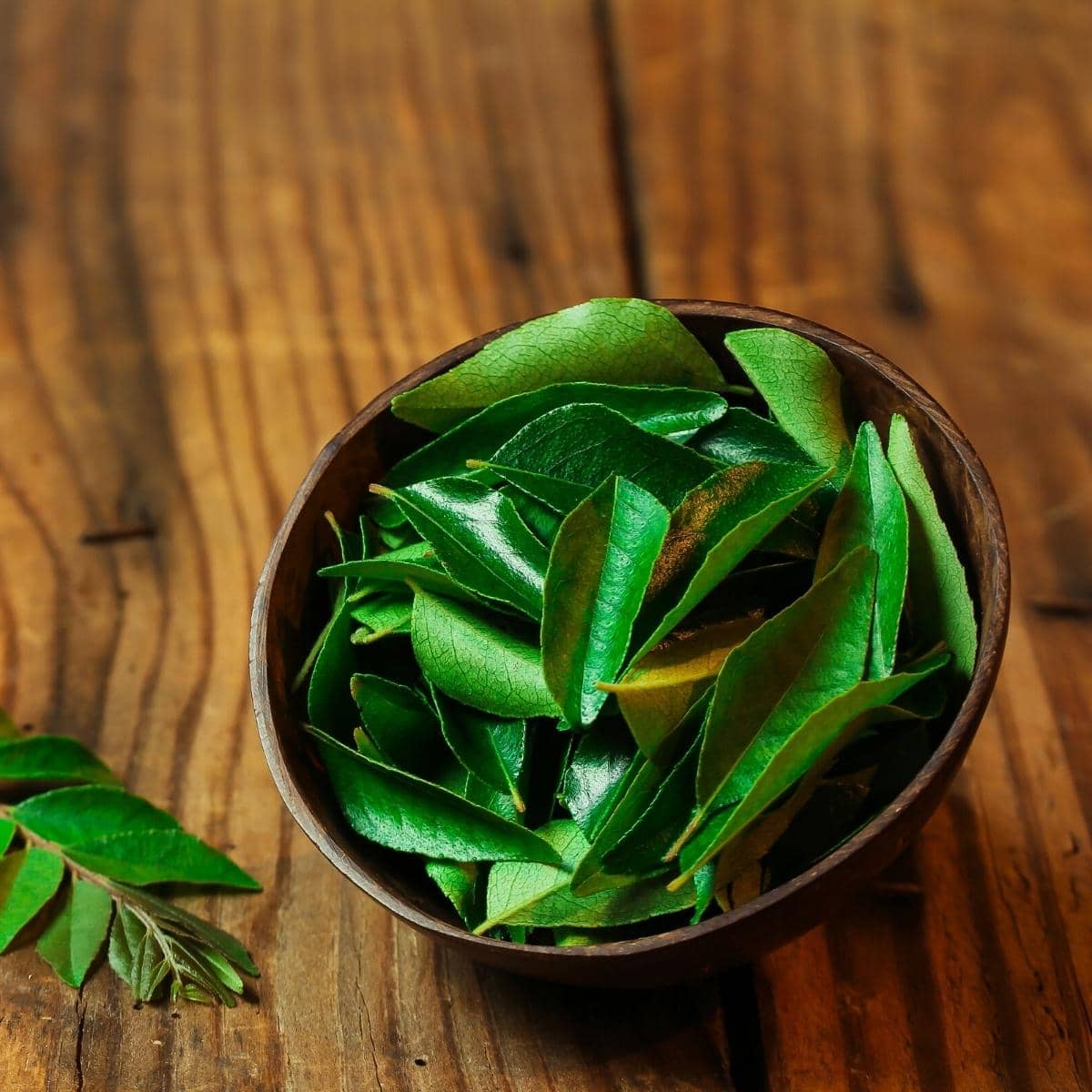 Green curry leaves resting in a round wooden bowl.