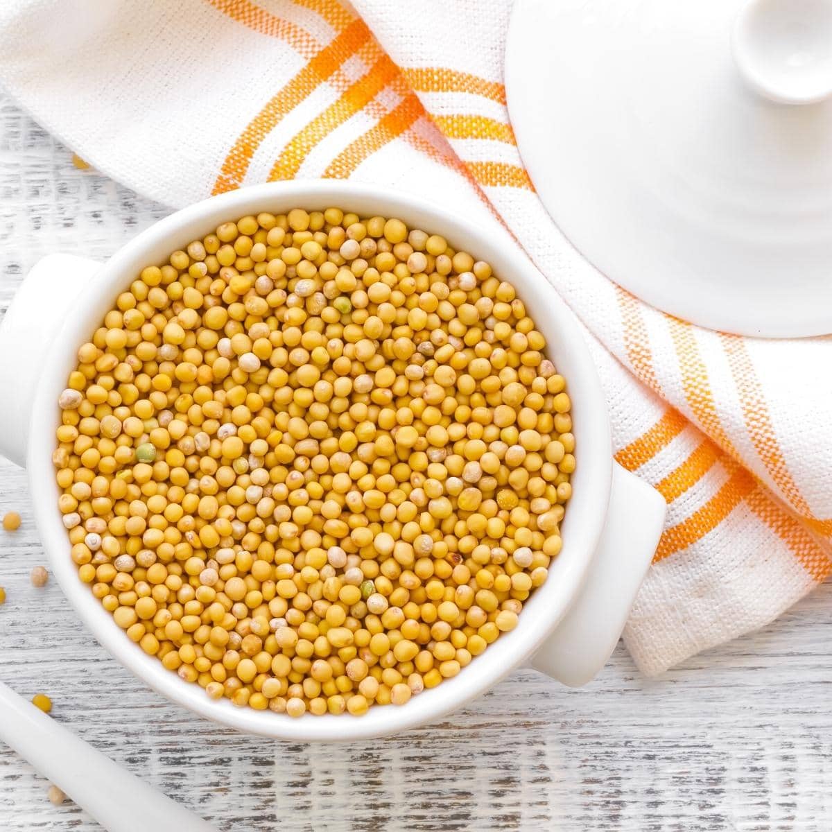 Yellow mustard seeds in a small white ceramic dish.