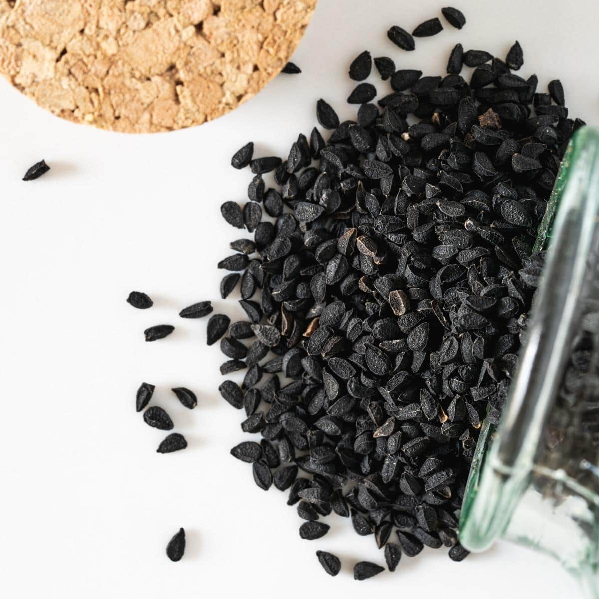 Black nigella seeds spilling out of a glass jar.