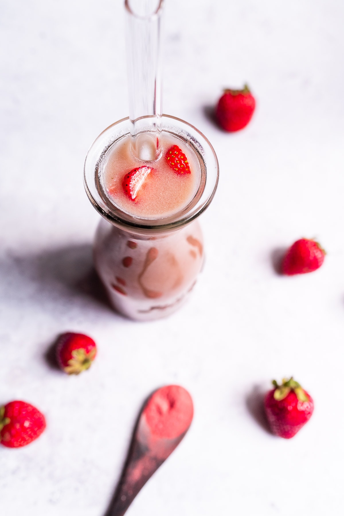 A large boba tea straw sticks out of a clear glass filled with a pink liquid and  freshly sliced strawberries.