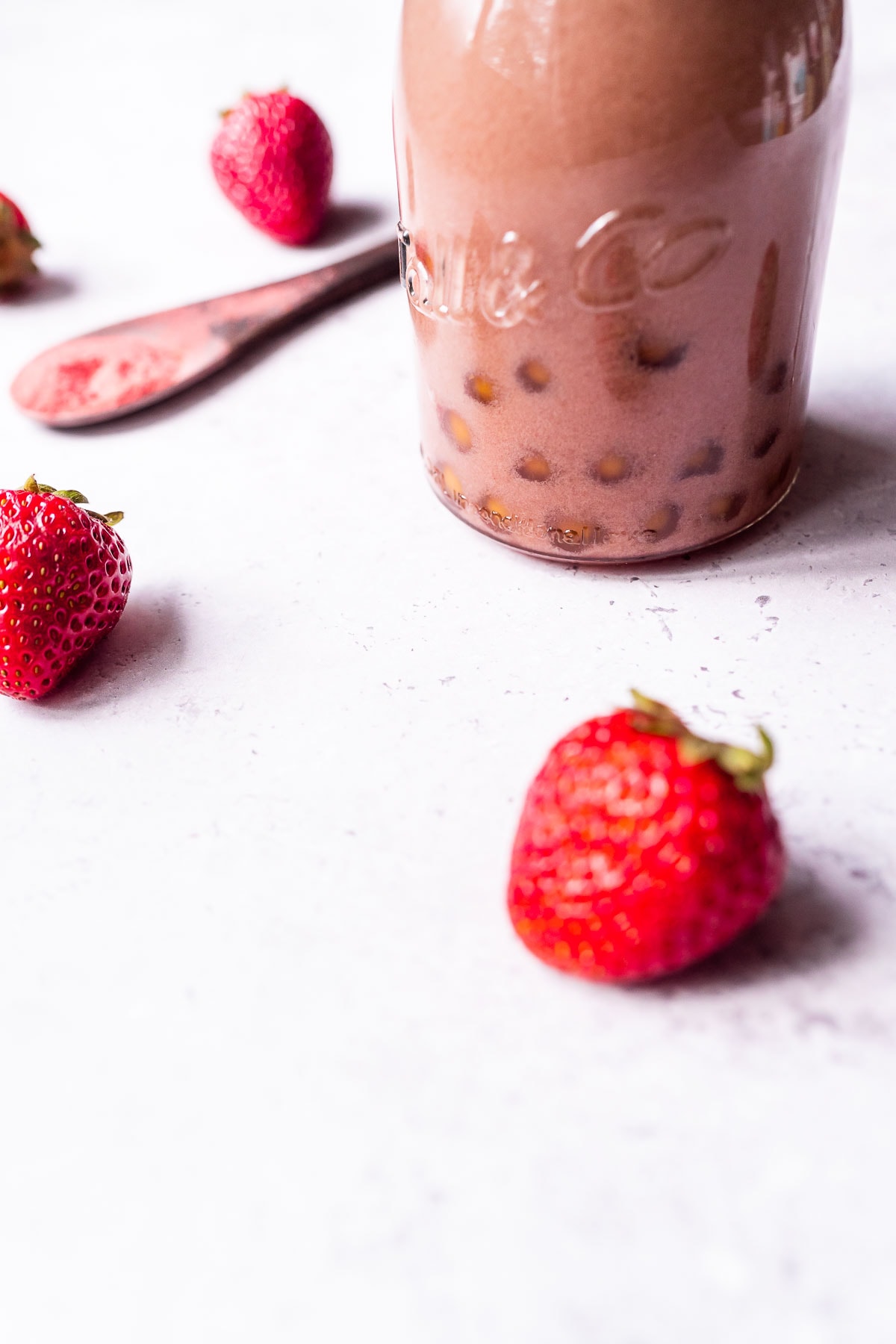 Strawberries scattered on a light grey table next to a bottle of strawberry bubble tea.