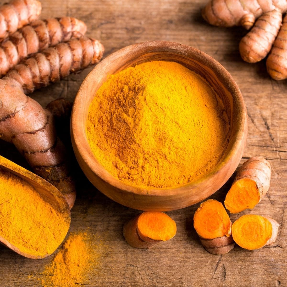 A wooden bowl filled with ground turmeric powder.