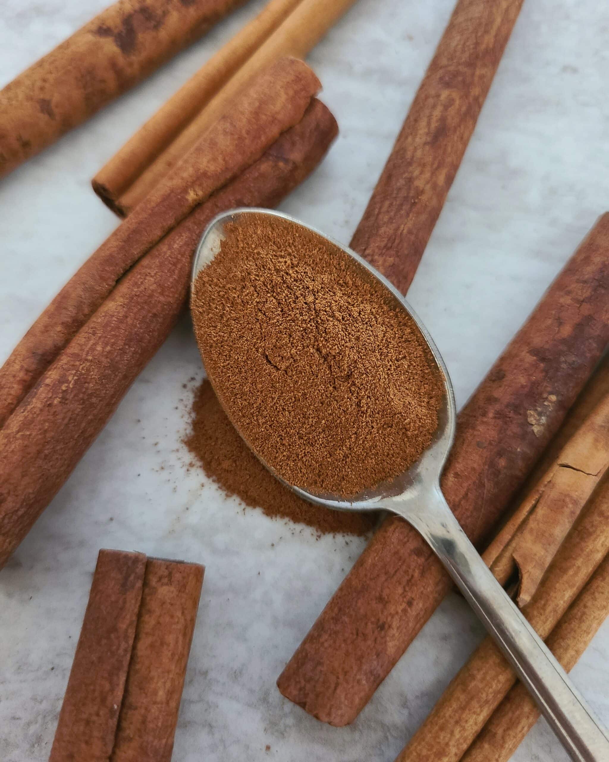 A silver spoon filled with ground cinnamon resting on a pile of cinnamon sticks.
