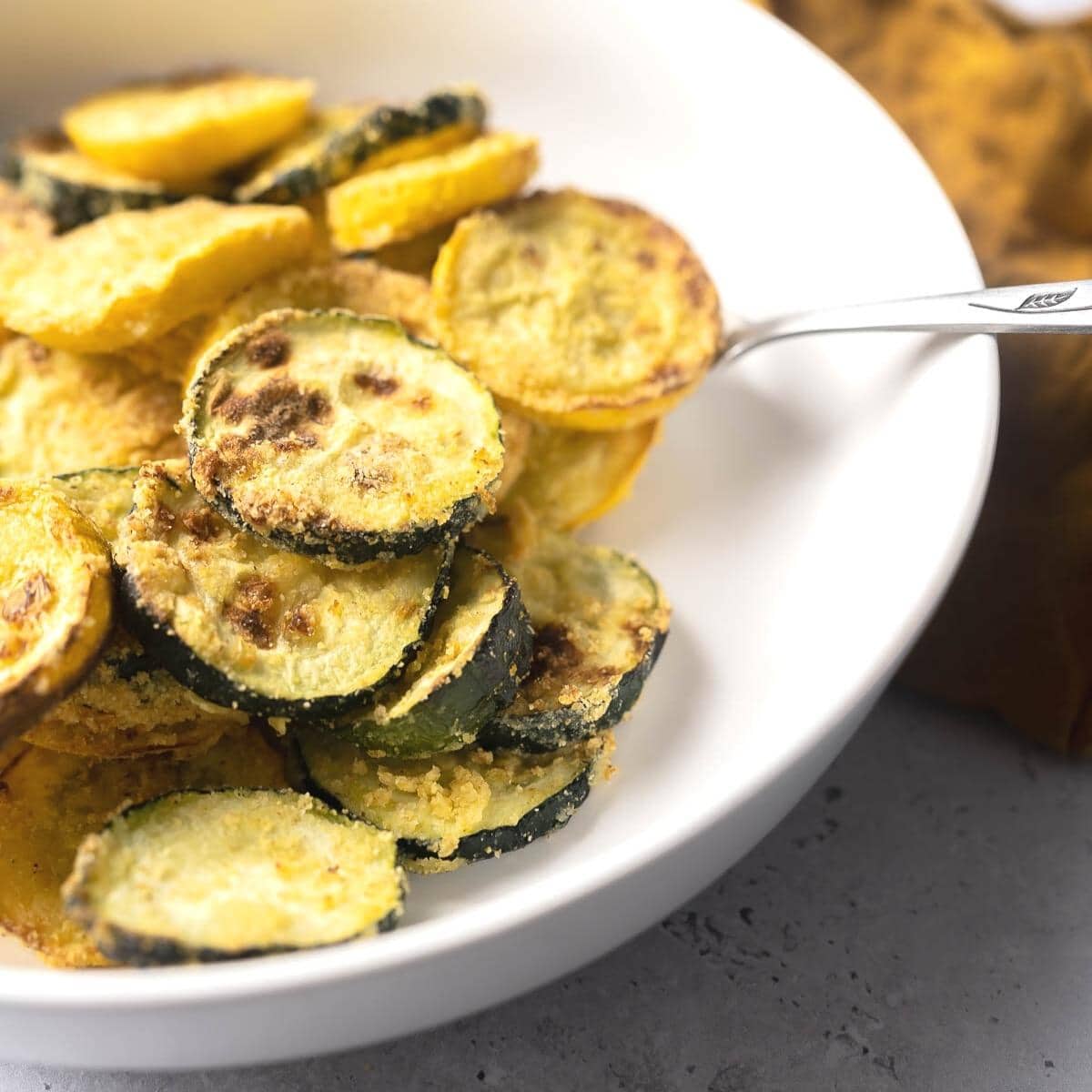 A silver fork cradles air fried summer squash in a white bowl.