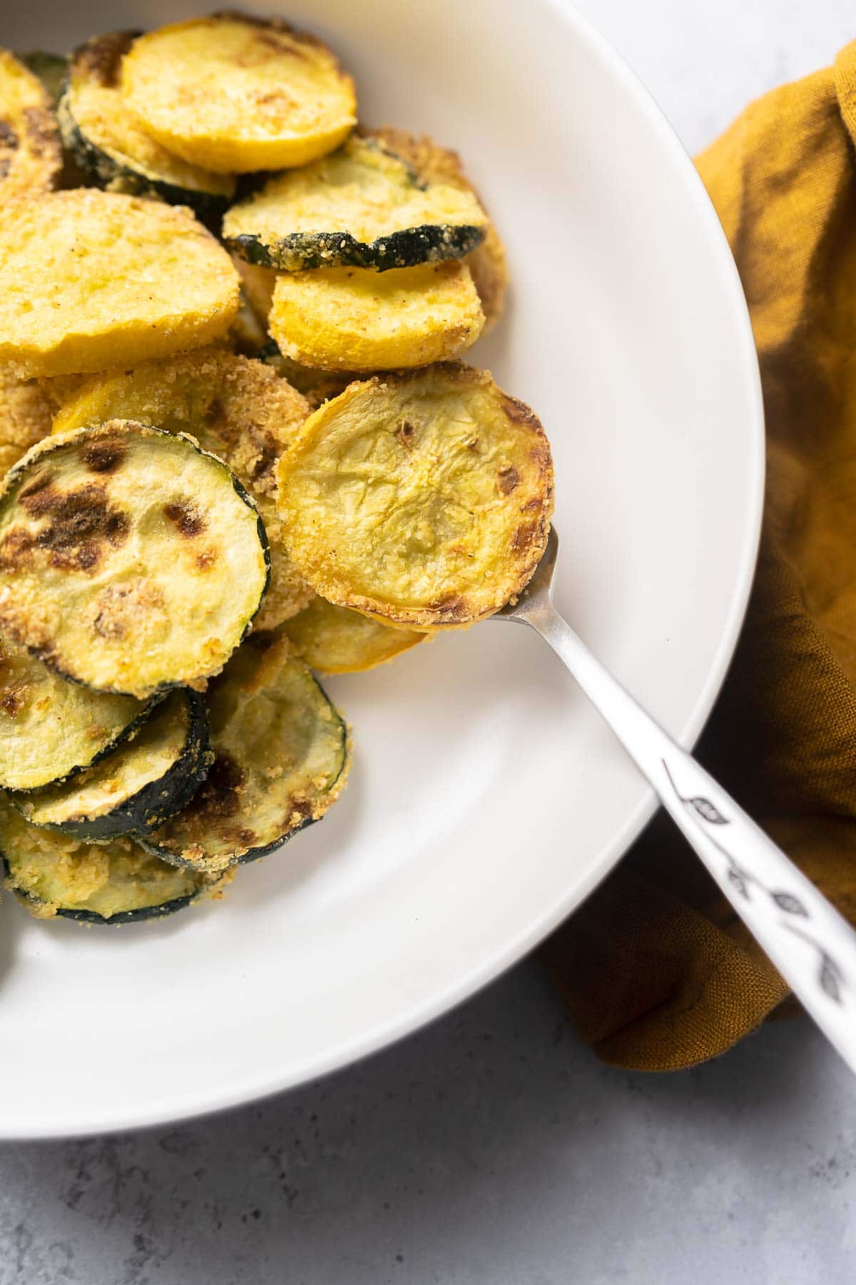 A silver fork holds a small thin slice of yellow squash.