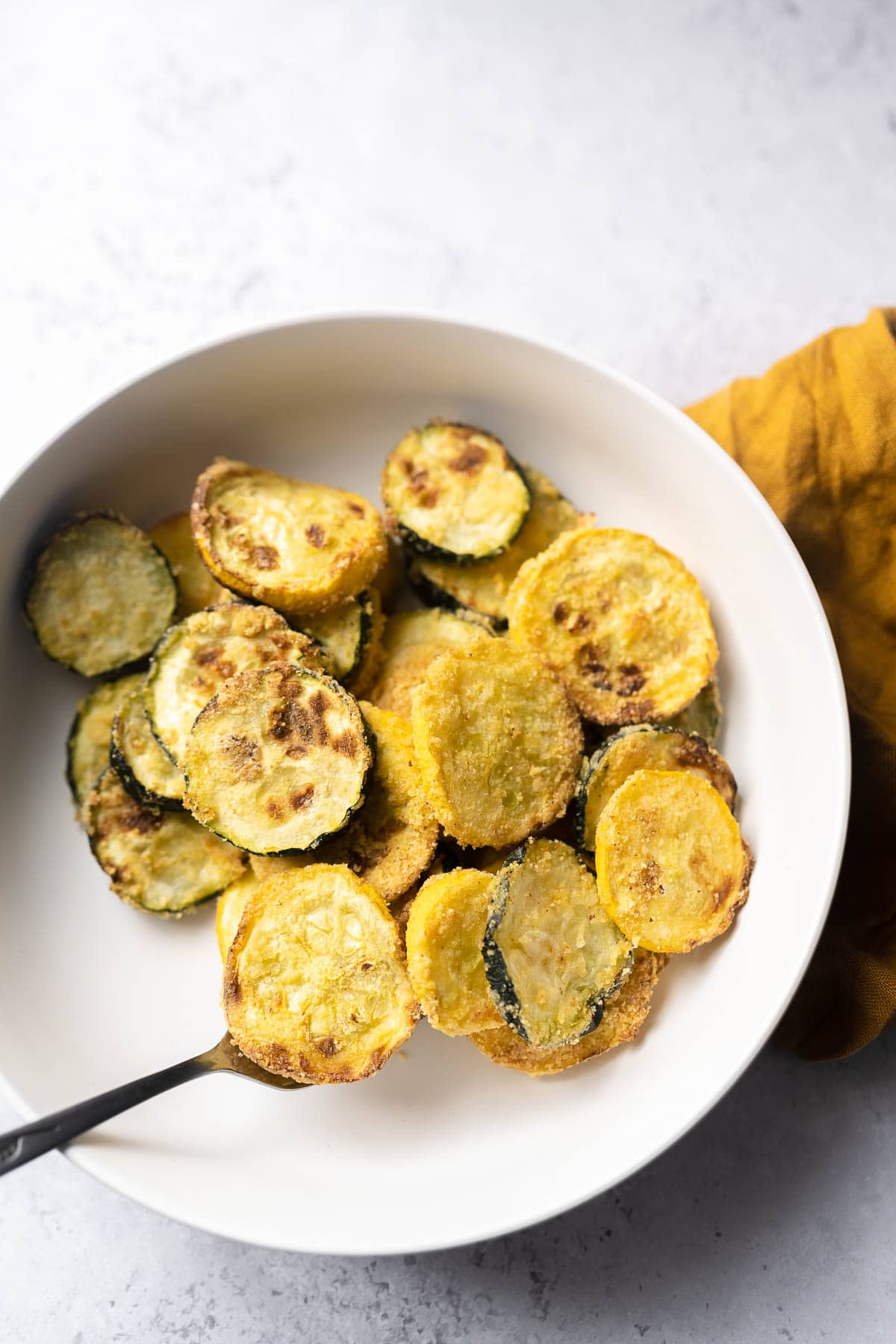 Top view of a white ceramic bowl filled with air fried yellow squash and green squash.