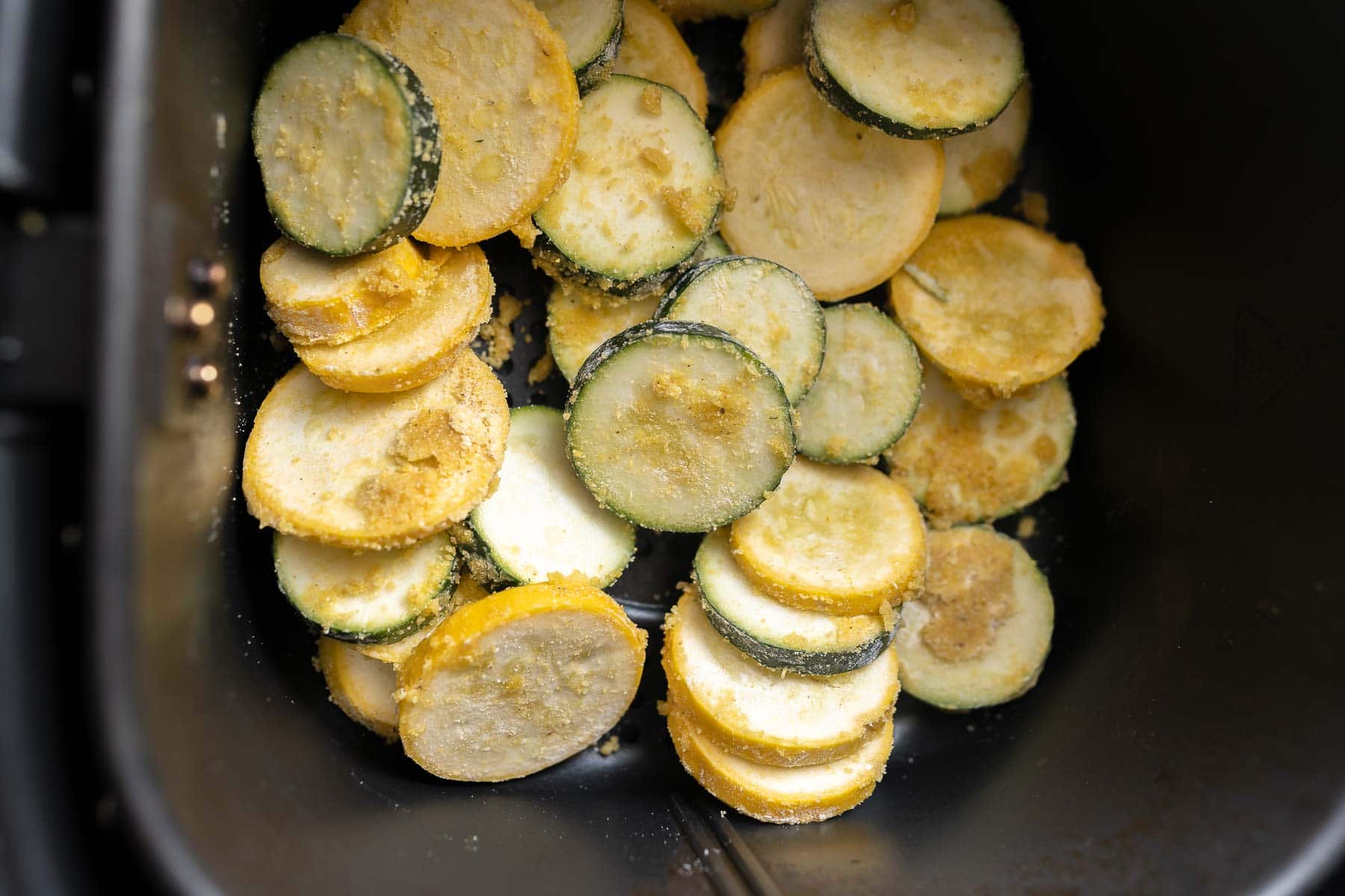 An air fryer basket filled with sliced summer squash.