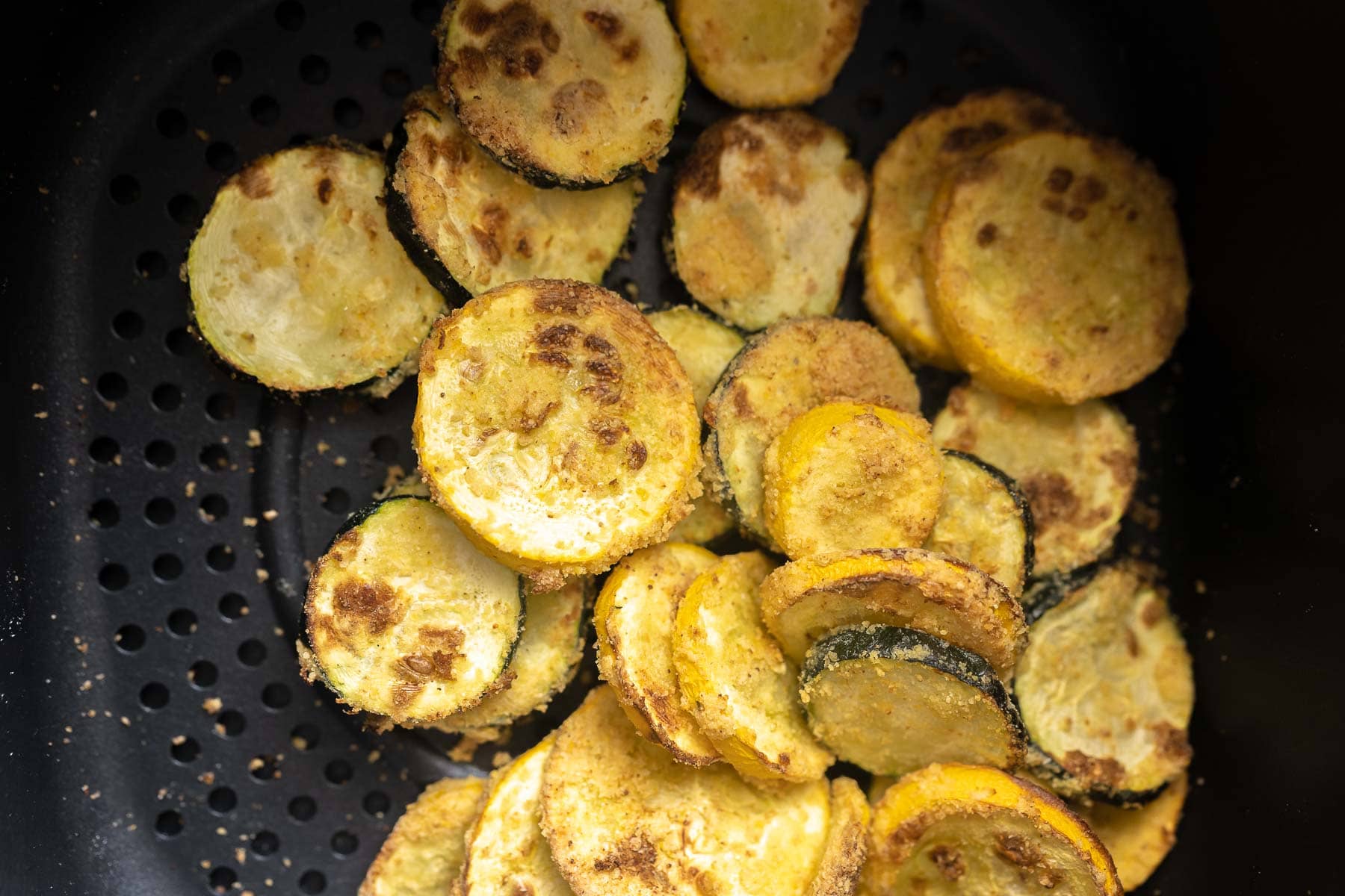 An air fryer basket filled with cooked, sliced squash.