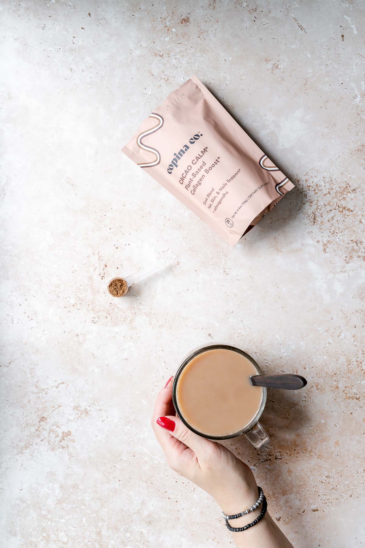 A hand holding a clear glass mug of copina co. cacao calm.