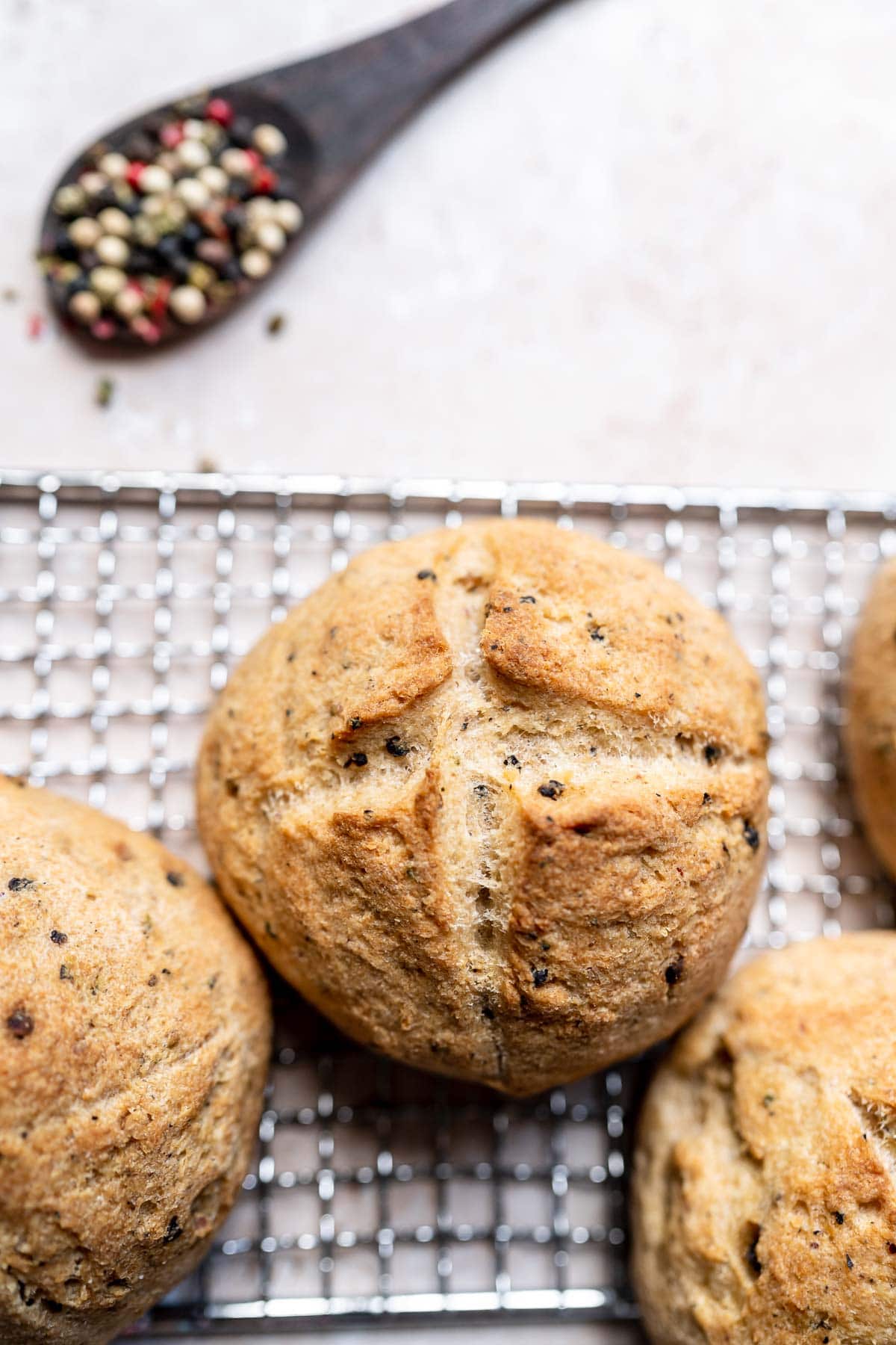 A close shot of a bread roll with an x marked on its top, speckled with black peppercorns.