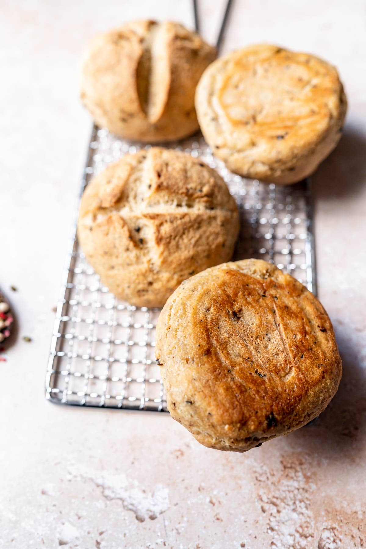 4 golden bread rolls, one turned over to show its bottom, resting on a metal silver cooling rack.