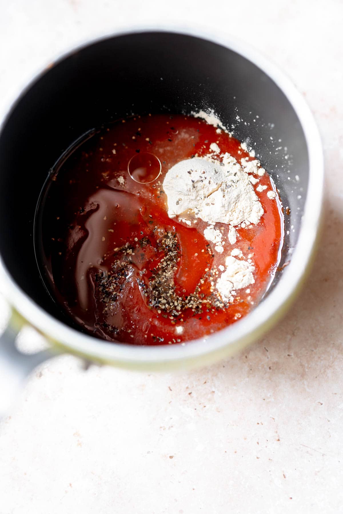 A saucepan filled with ingredients like red hot sauce, garlic powder, black pepper and honey.