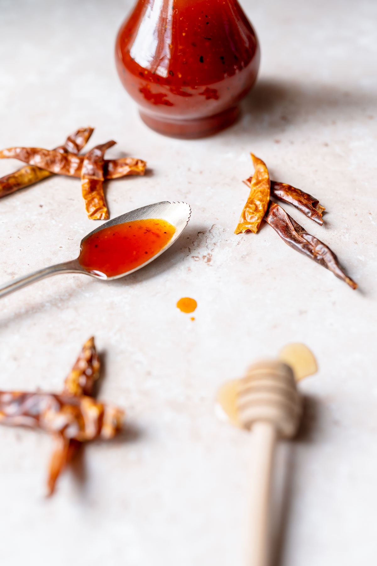 A silver spoon dripping with red sauce rests next to piles of dried chiles.