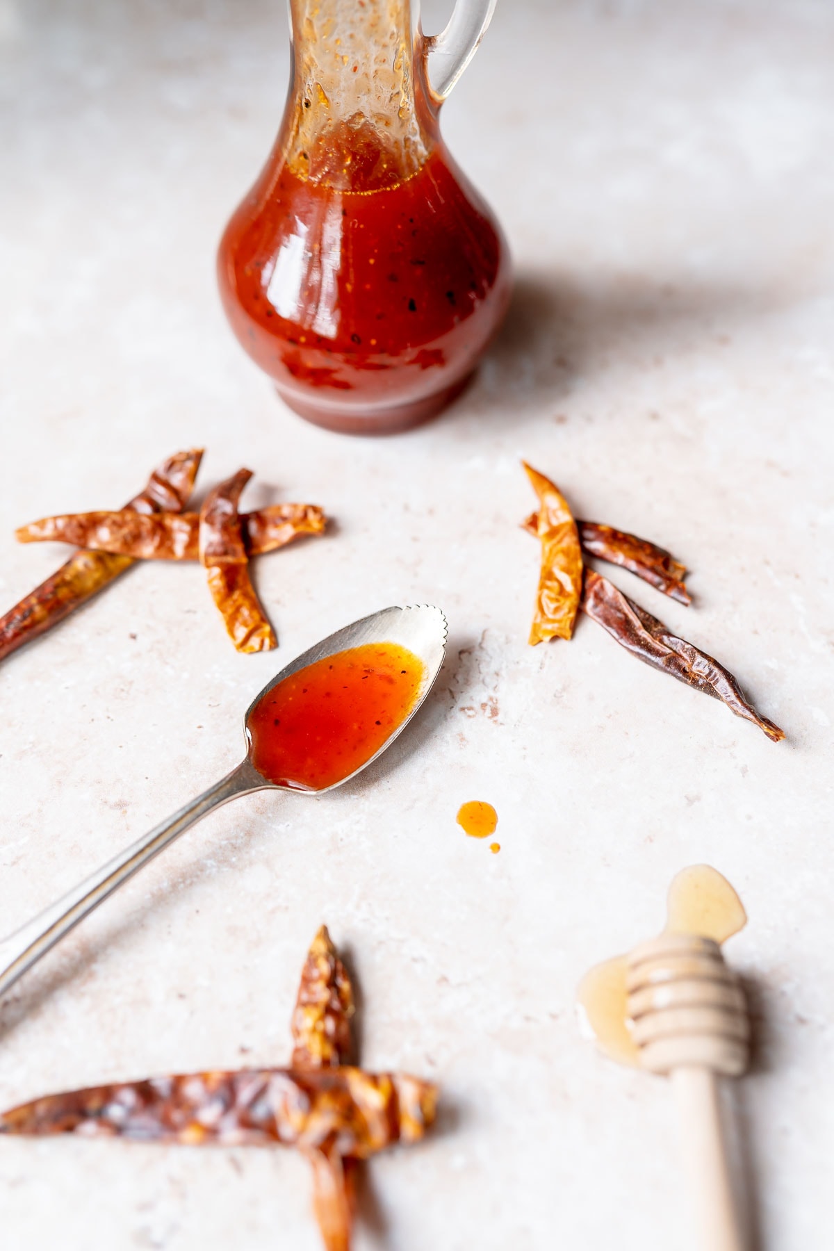 A silver spoon filled with red sauce rests on a light colored table next to dried chili peppers.