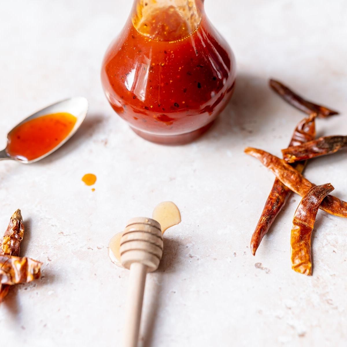 A wooden honey spoon rests in front of a clear glass bottle of red sauce.