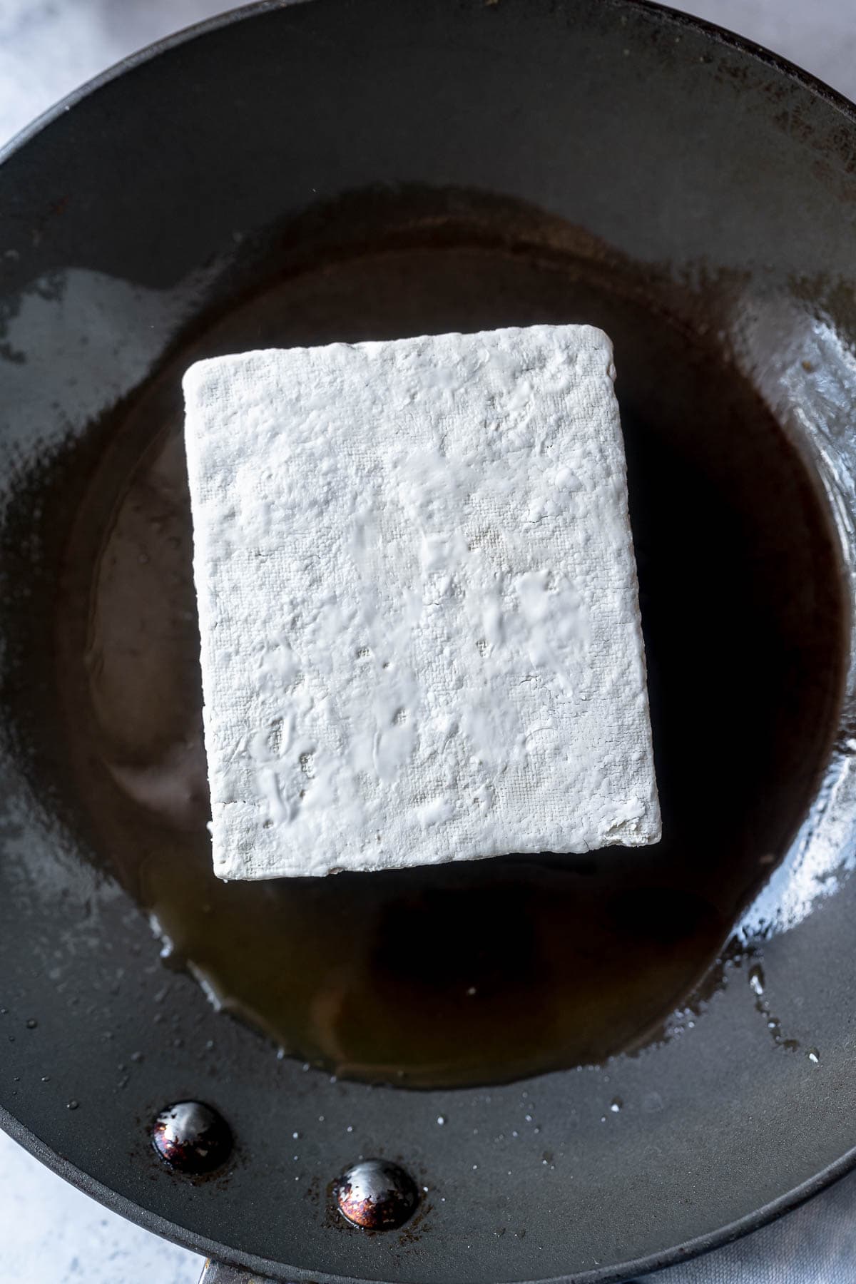 A block of tofu sitting in an oiled skillet