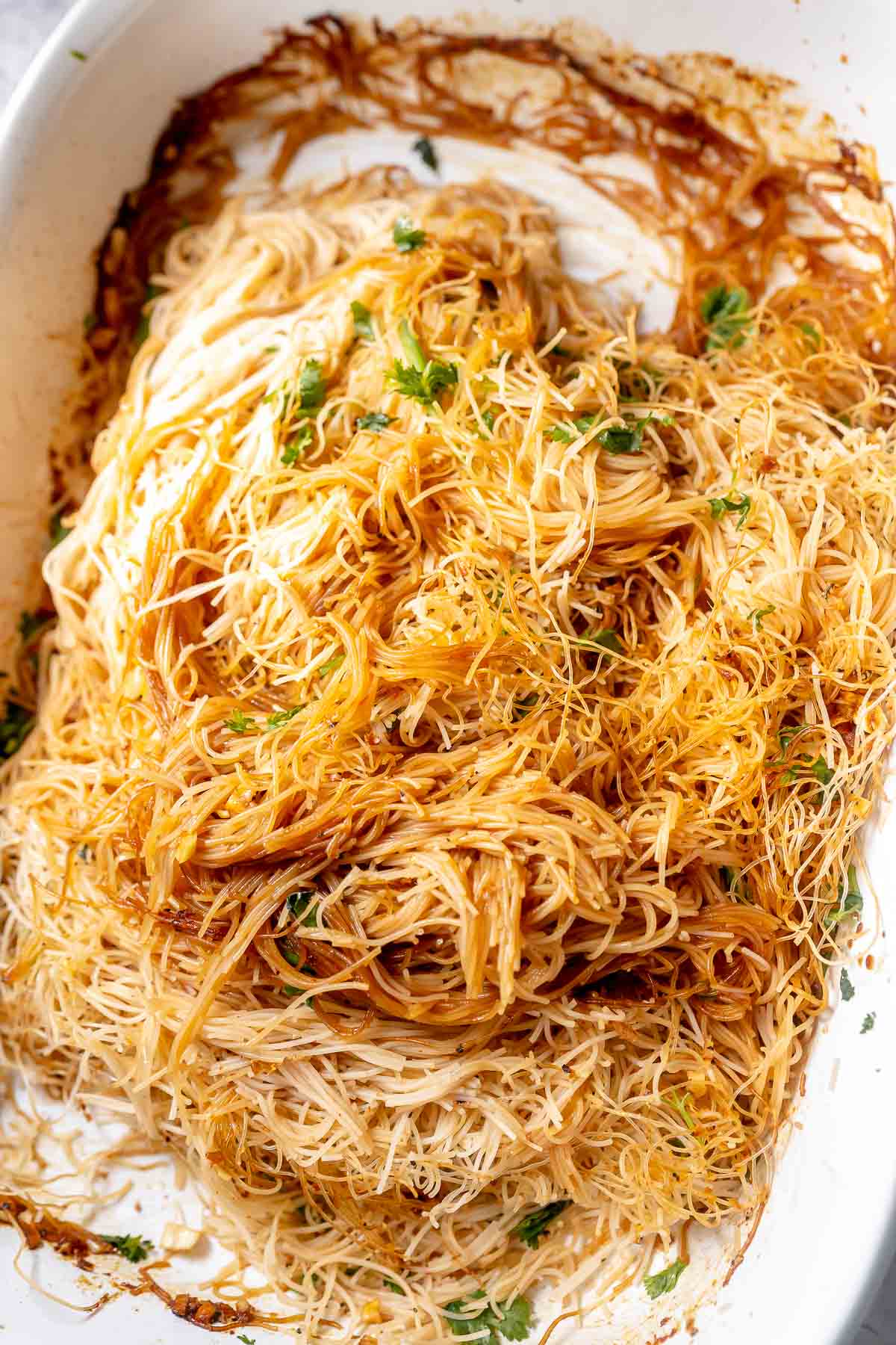 A bundle of cooked brown noodles in a large white ceramic baking dish.