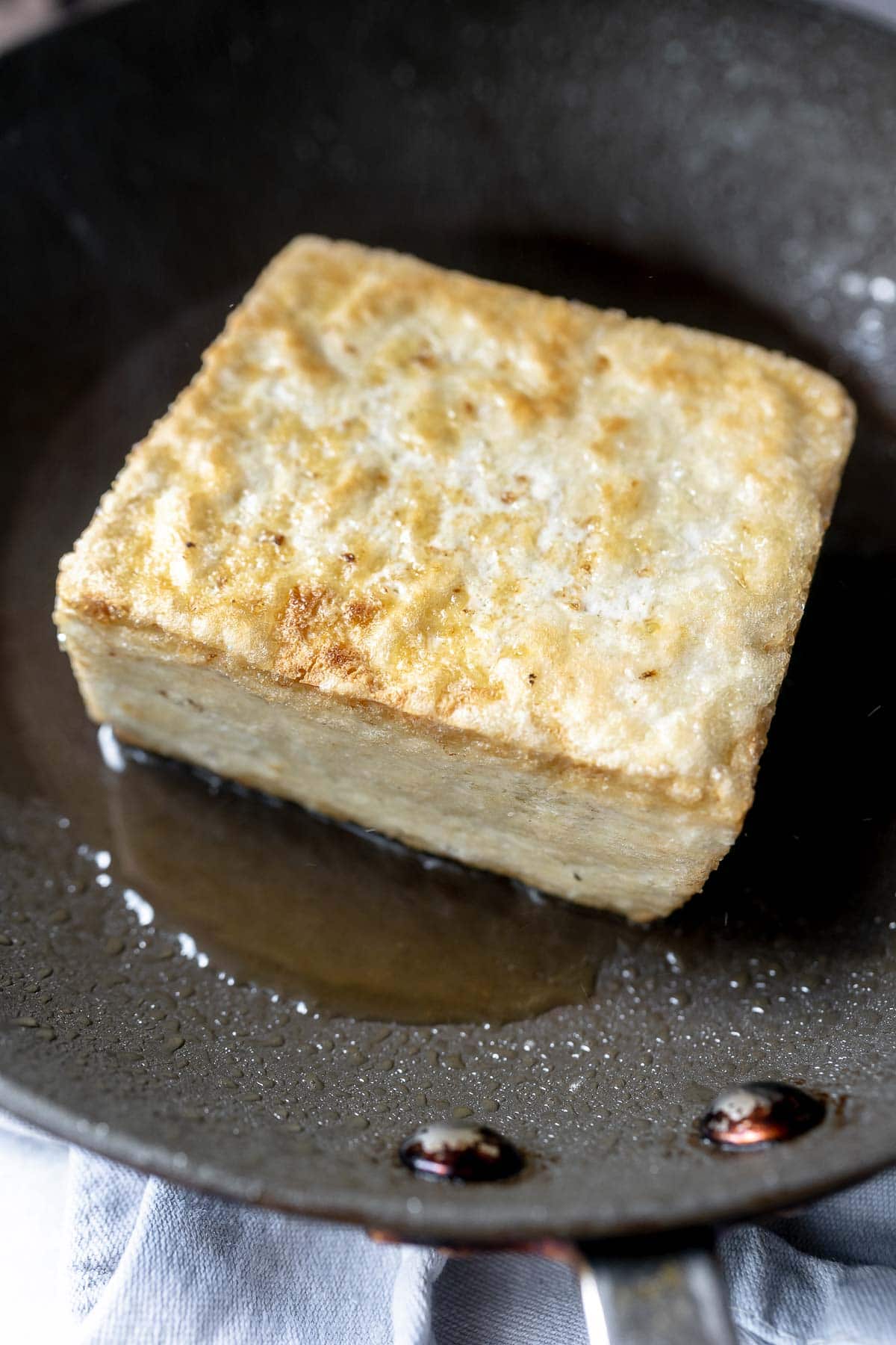 A browned block of tofu sitting in an oiled skillet.