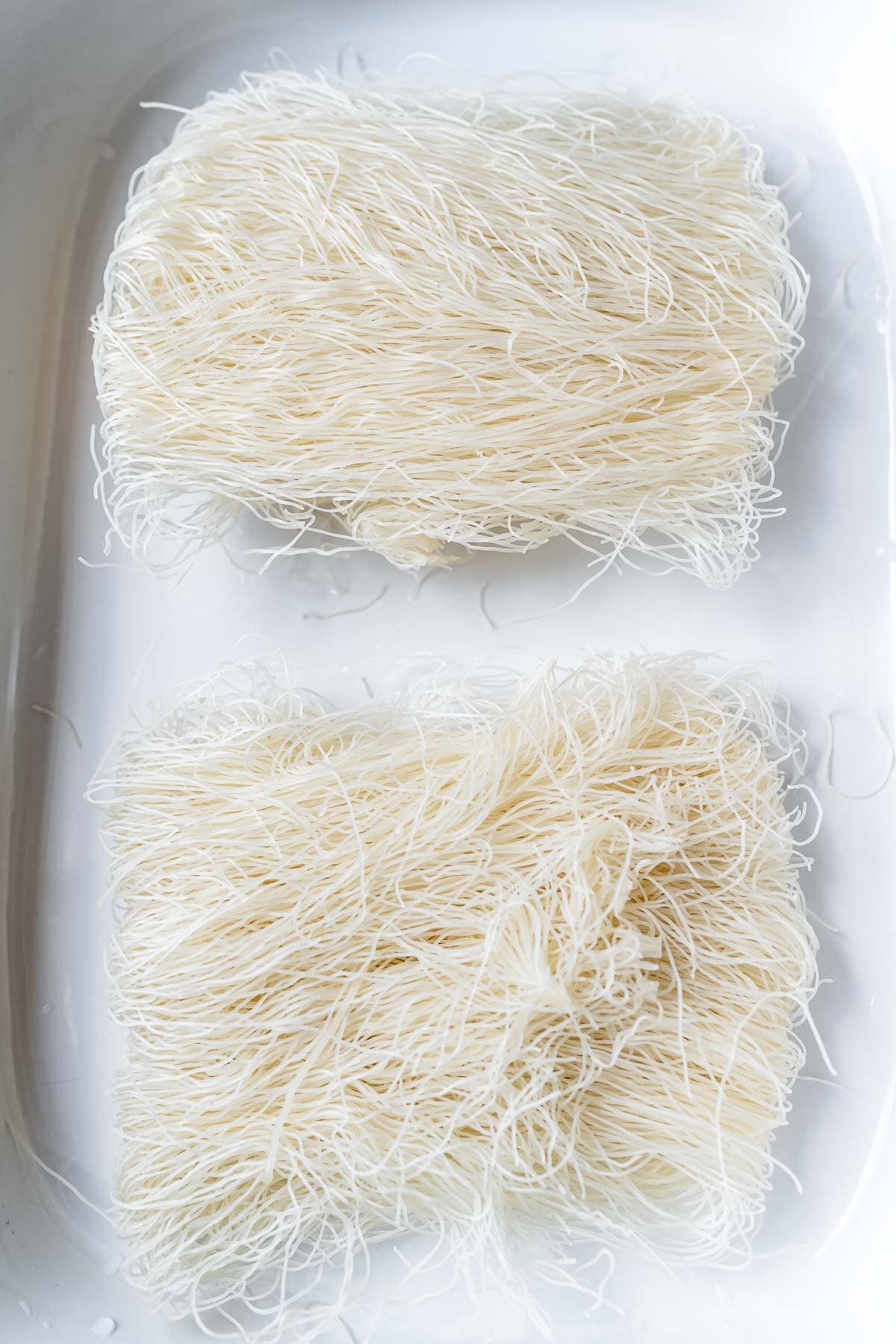 Dried thin noodles resting in a large white baking dish.