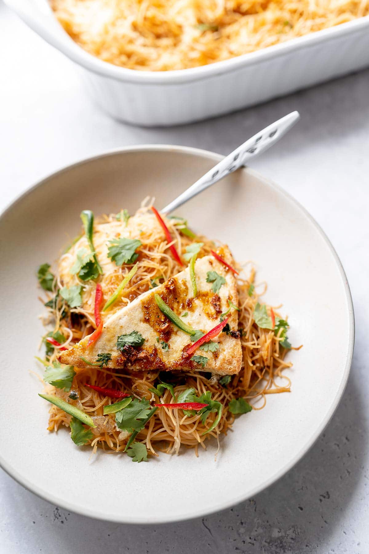 A tan ceramic bowl filled with thin noodles, tofu and sliced peppers.